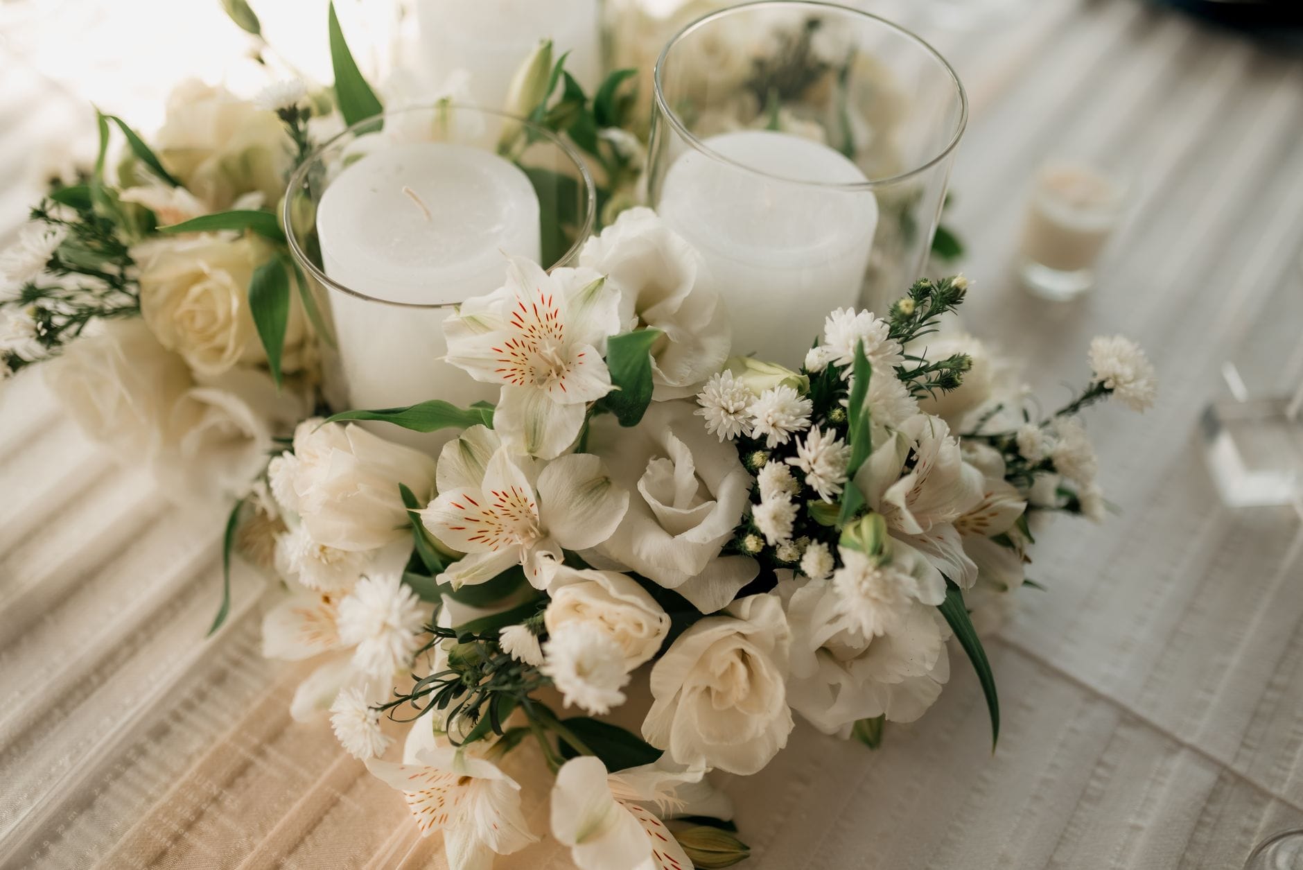 A centerpiece featuring white candles in glass holders surrounded by white flowers on a table.